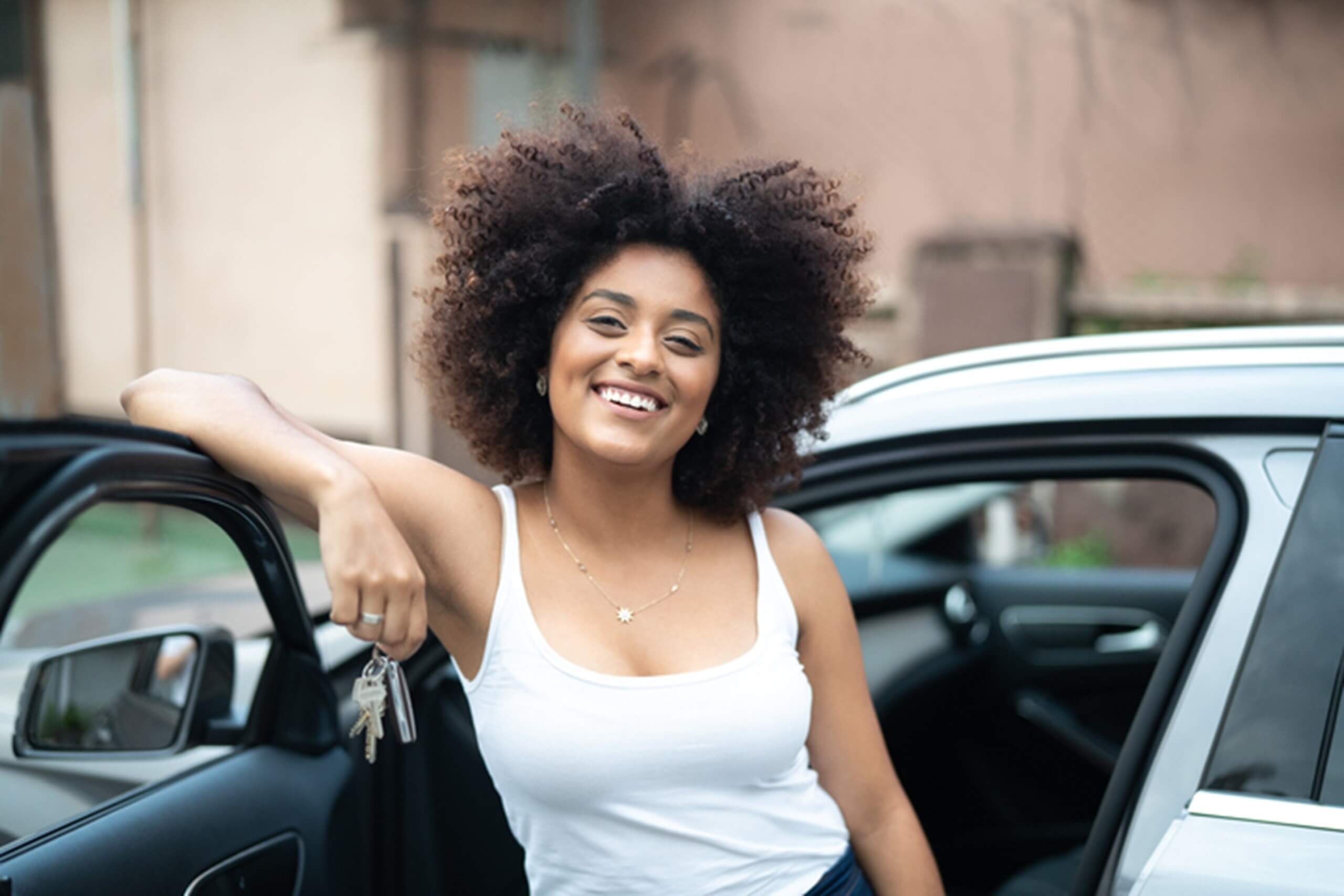 Jovem mulher sorri segurando chaves do carro